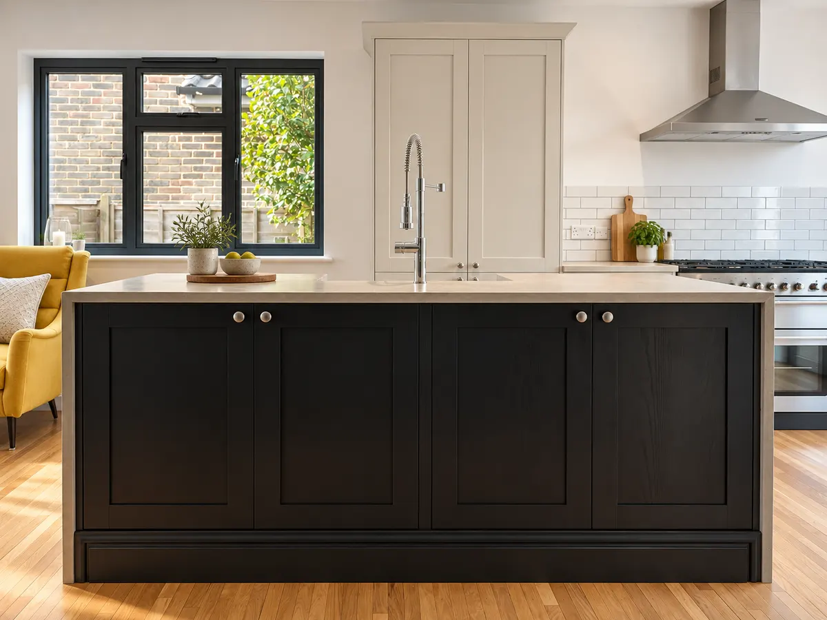 Dark shaker island with knob handles and a pale concrete top, larder units and range cooker beyond