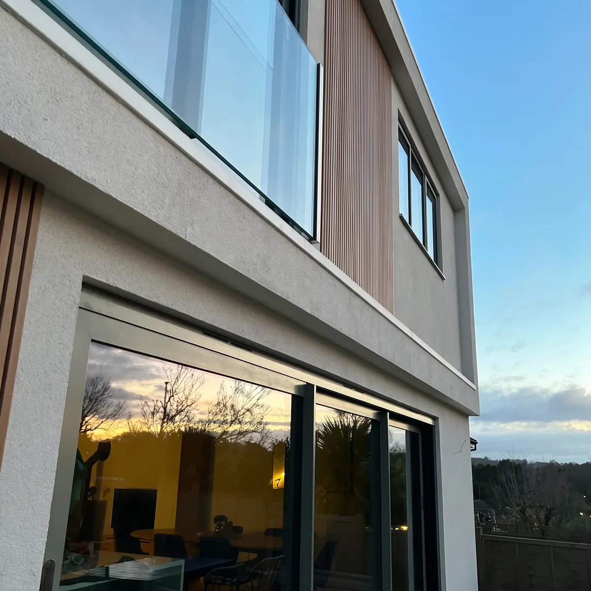 Modern two storey rear extension with render, timber cladding, sliding doors and a glass balcony