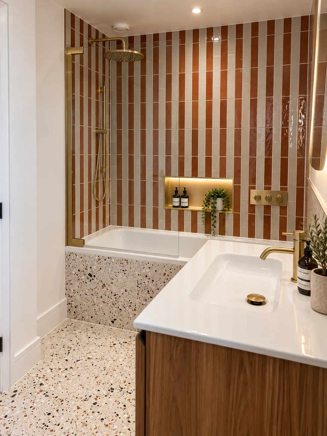 Walnut vanity with a white basin and brass tap beside a terrazzo panelled bath