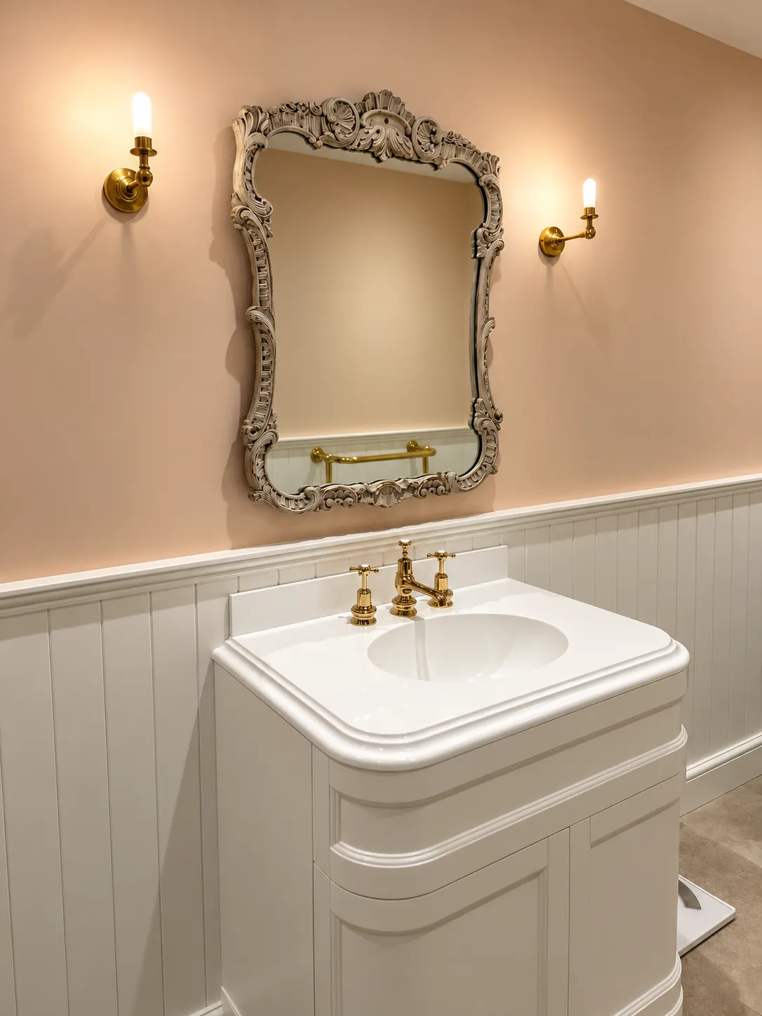 White curved basin unit with brass taps under a carved mirror and two brass wall lights