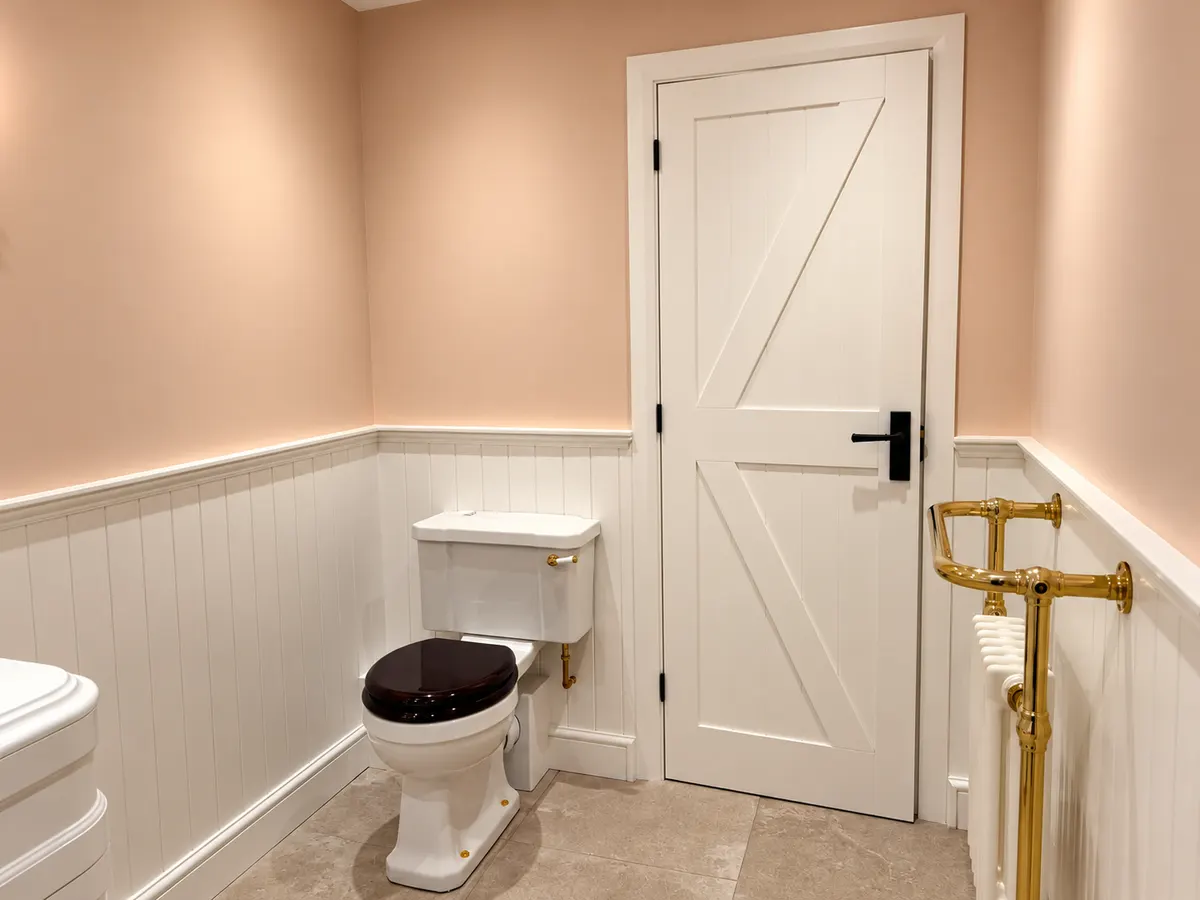 Traditional close coupled WC, ledged and braced door and a polished brass towel radiator against panelling